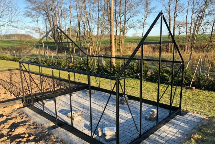 Partially assembled black aluminium greenhouse frame on a paved base in a garden  Copy