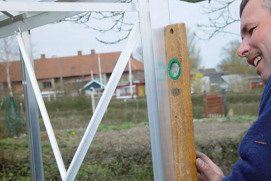 Person checking the alignment of an aluminium greenhouse frame with a spirit level  Copy